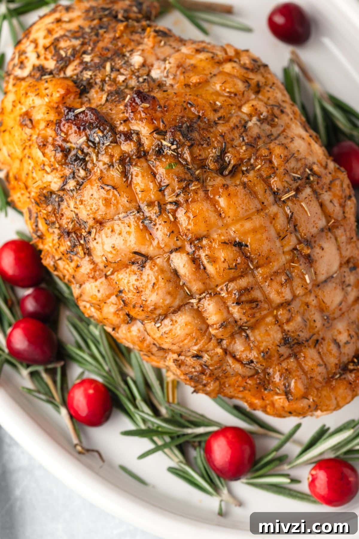 Roasted Turkey Breast on a white platter with fresh rosemary and cranberries beside it.