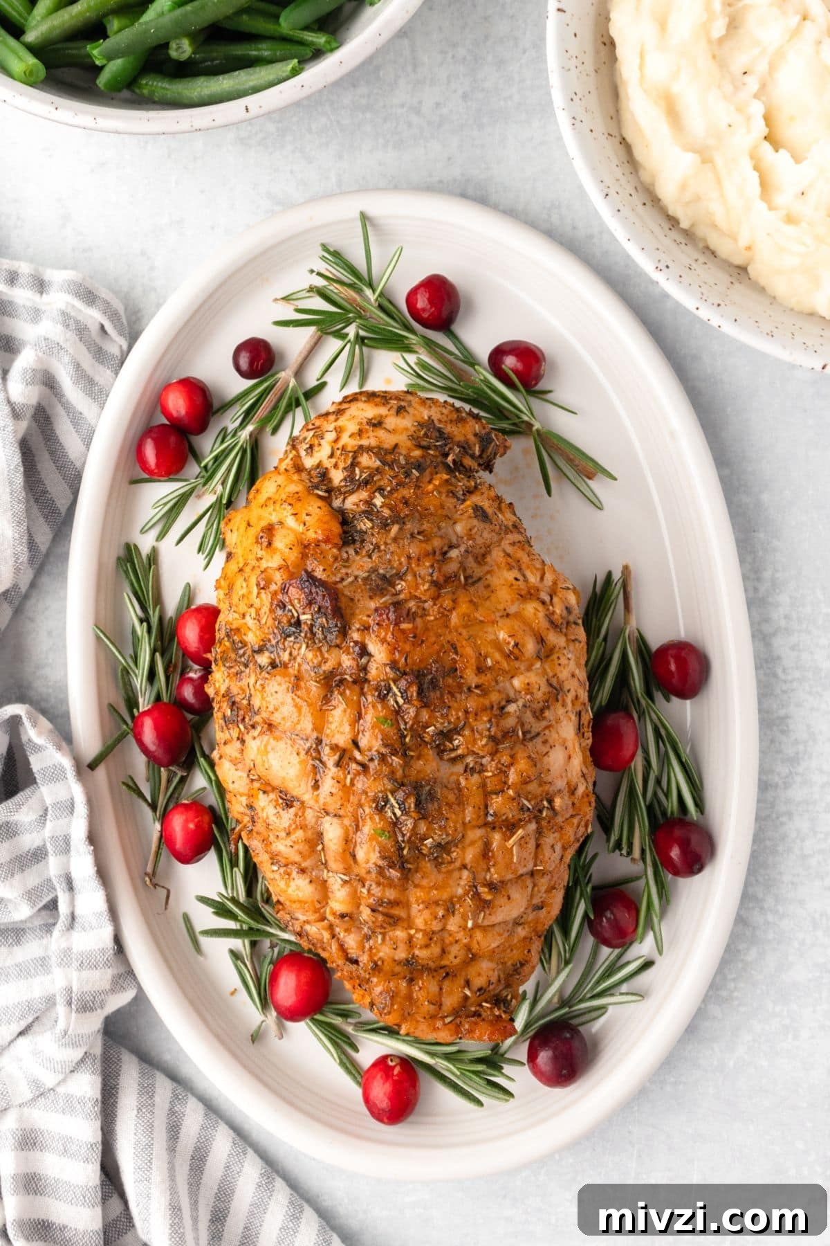 Succulent roasted herb-crusted chicken breast garnished with rosemary and cranberries on a white platter.