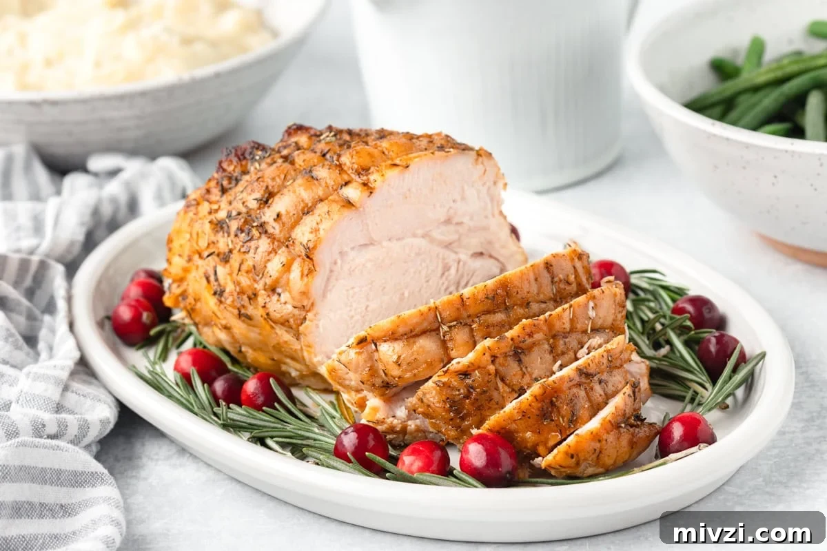 Juicy roasted turkey breast garnished with cranberries and rosemary on a white platter.