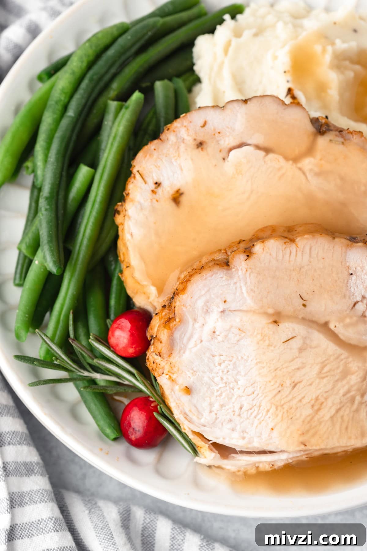 Close up view of sliced boneless turkey breast with gravy and green beans.