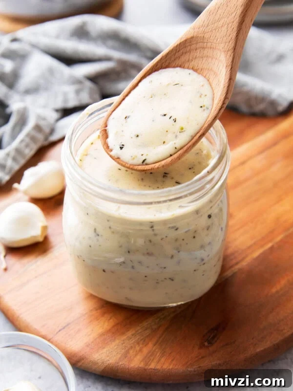 A wooden spoon filled with garlic parmesan sauce to showcase its thick and creamy texture that’s perfect for pouring over pasta, as a pizza sauce, and as wing sauce."