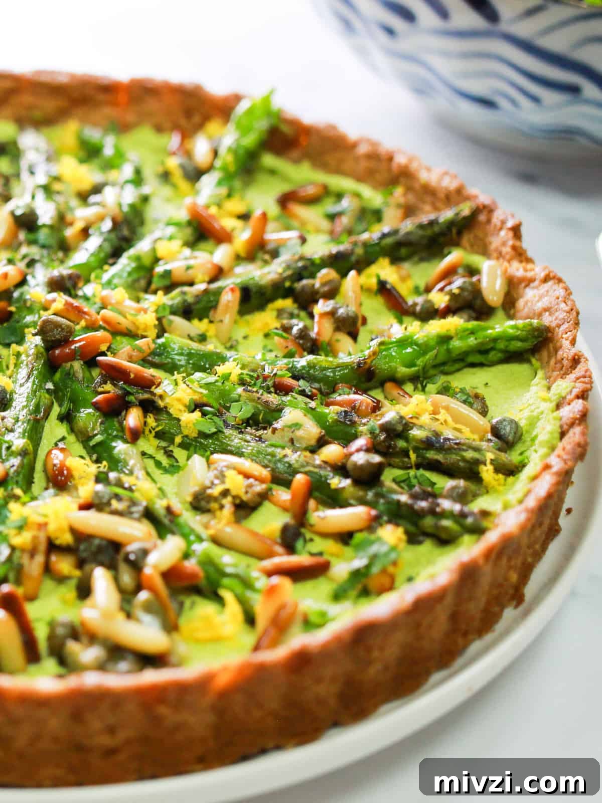 close-up photo of half of a whole vegan asparagus tart with pesto macadamia filling.