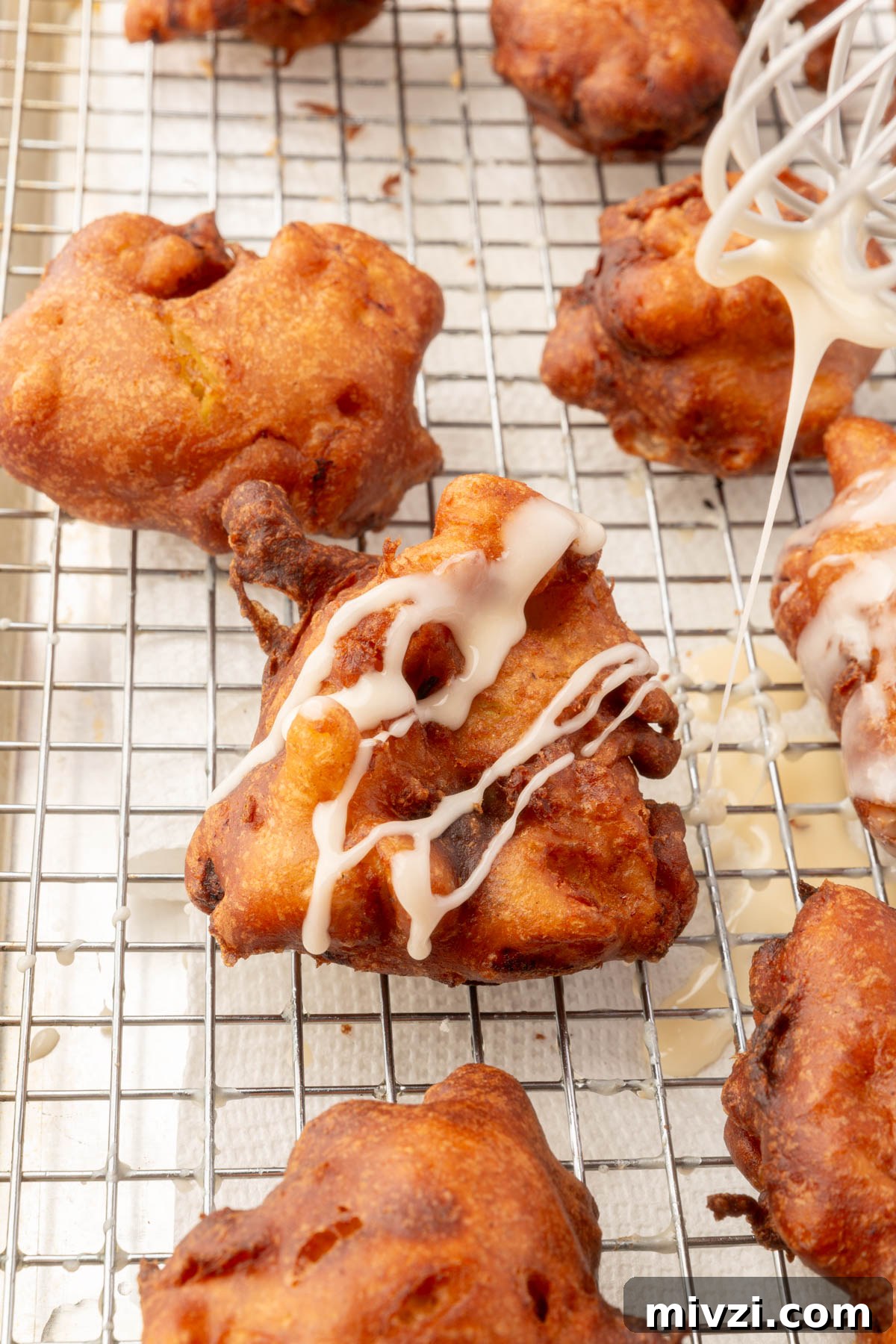 Crispy Gluten-Free Apple Fritters Recipe 13 Drizzling glaze over freshly fried gluten-free apple fritters on a cooling rack.