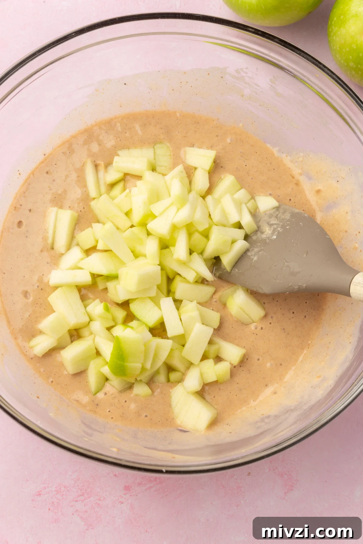 Crispy Gluten-Free Apple Fritters Recipe 9 A glass mixing bowl with gluten-free apple fritter batter topped with diced granny smith apple before mixing together.