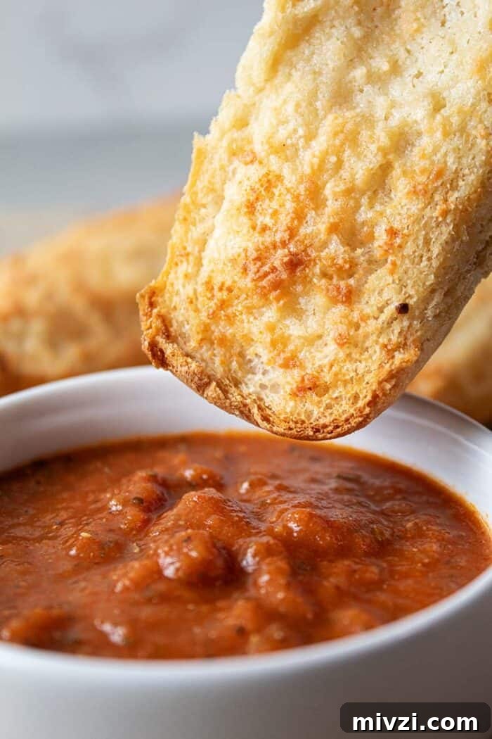 sideview of easiest low carb garlic bread being dipped into white bowl with marinara dipping sauce